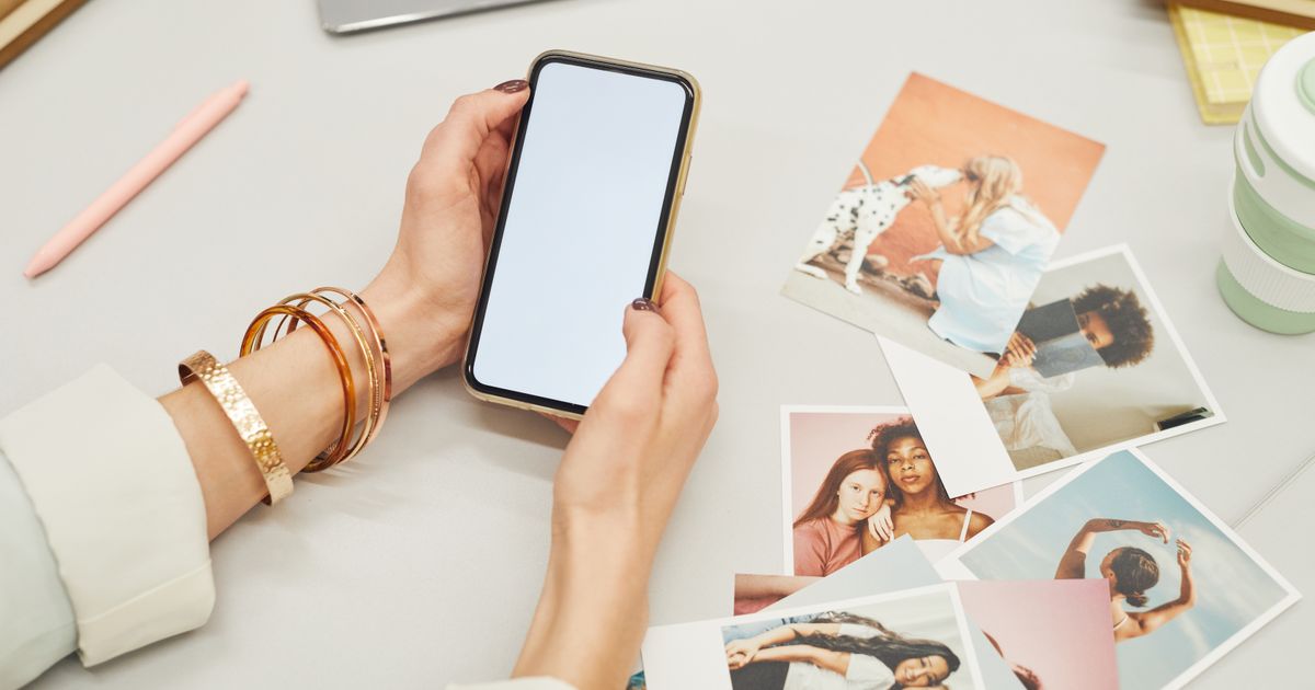 Mãos segurando um celular ao lado de fotos impressas sobre uma mesa