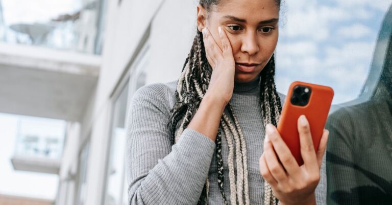 Mulher olhando o celular preocupada ao perder o acesso a conta