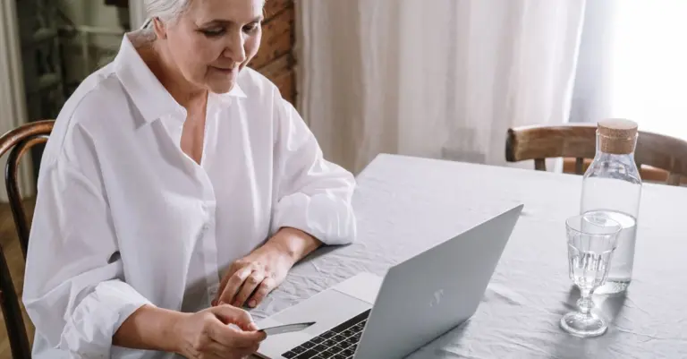 Mulher madura usando o notebook e segurando um cartão em casa
