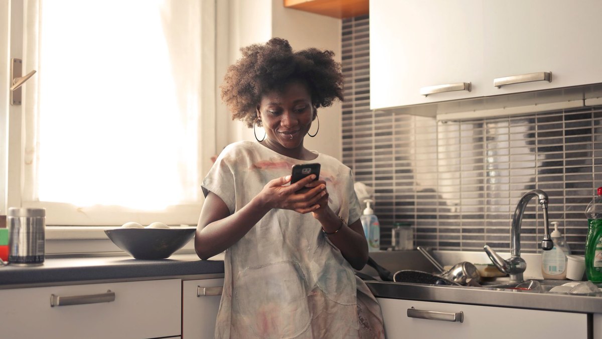 Mulher em casa consultando o celular para verificar as condições do cartão de crédito