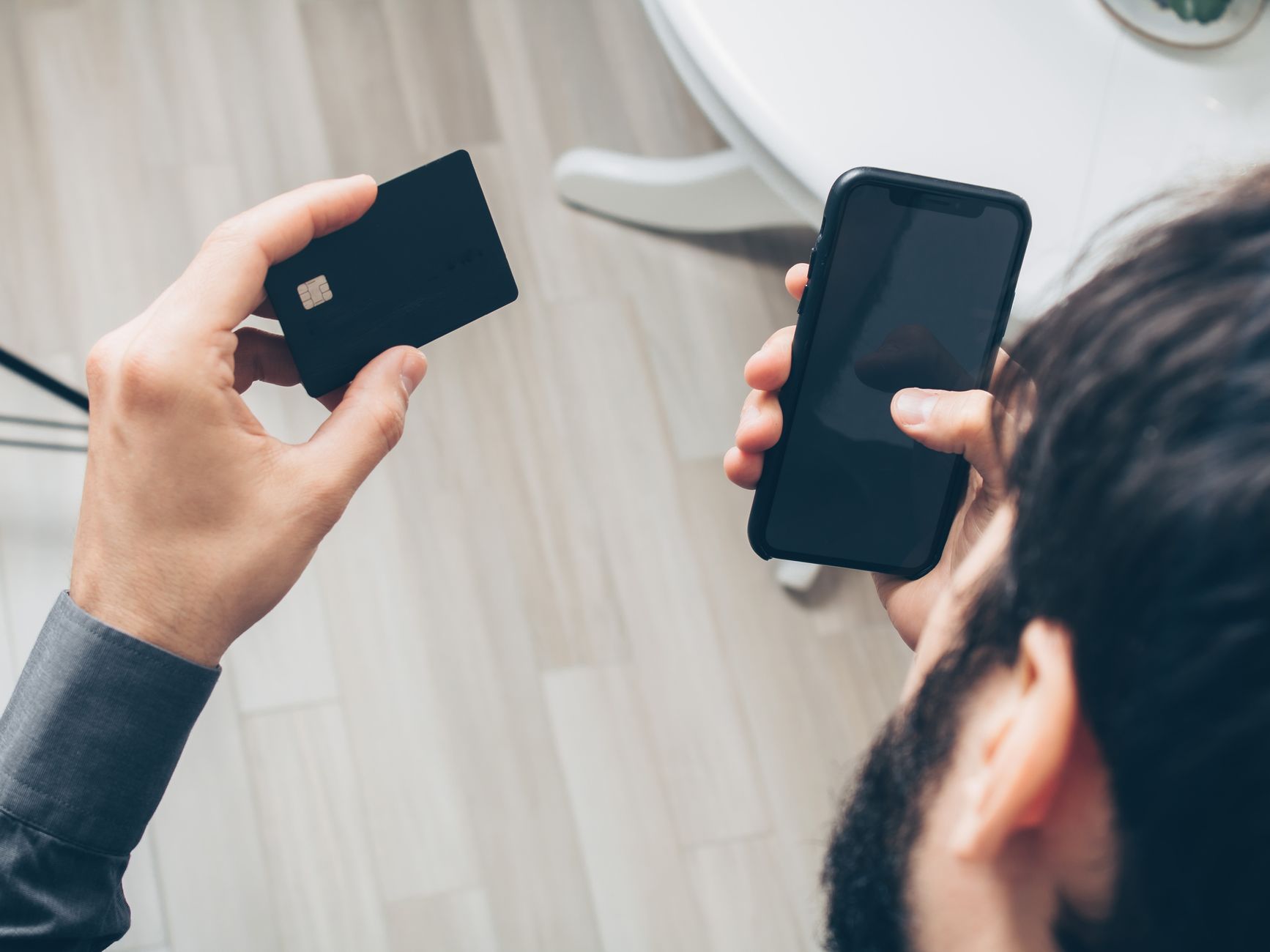 Pessoa segurando um cartão e o celular para verificar o pedido do cartão de crédito pelo aplicativo
