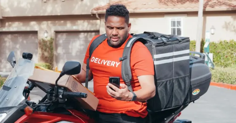 Entregador de aplicativo na moto conferindo o pedido no celular