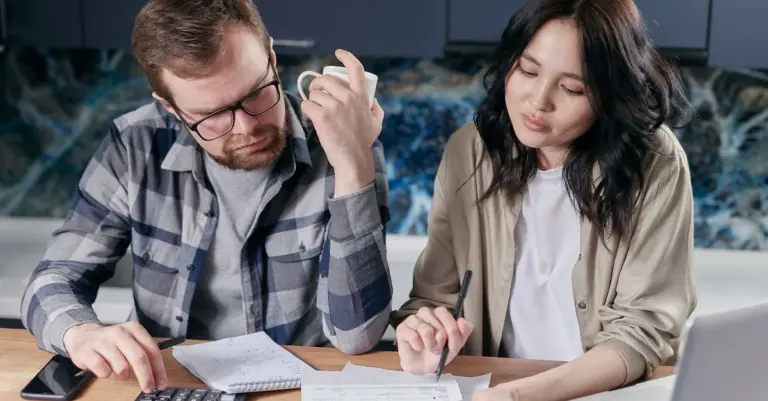 Casal organizando contas com calculadora e notebook em casa