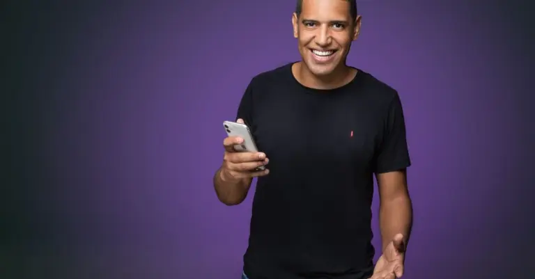 Homem sorrindo segurando o celular em fundo roxo