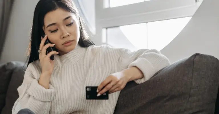 Mulher ao telefone segurando um cartão de crédito no sofá