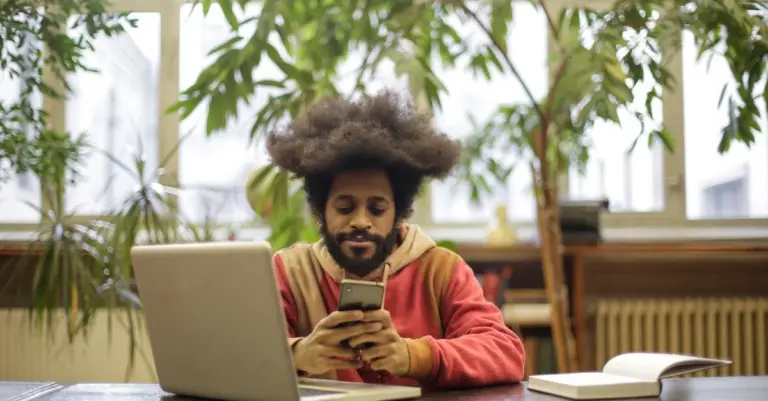 Homem na mesa com notebook e celular comparando opções