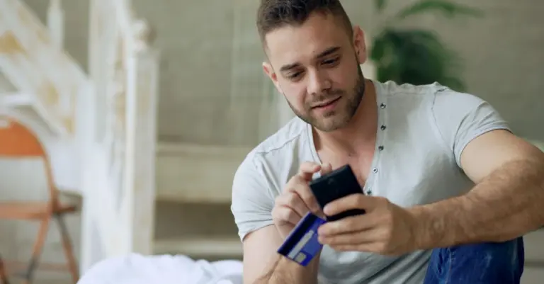 Homem sorrindo com celular e cartão de crédito