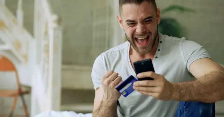 Homem comemorando com celular e cartão de crédito