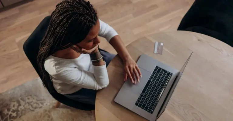 Mulher pensativa diante do notebook com um cartão na mesa