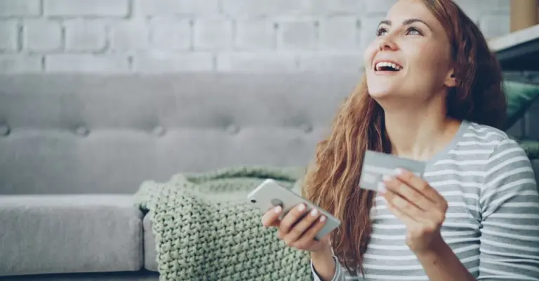 Mulher alegre segurando o celular e um cartão de crédito