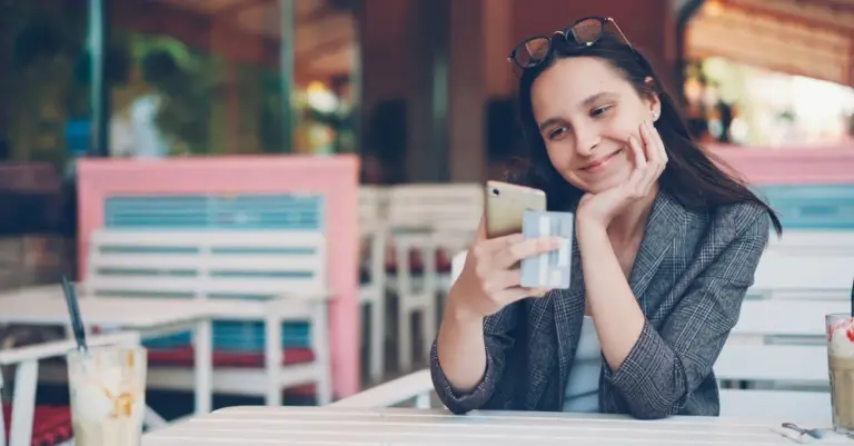 Mulher sorrindo com celular e cartão em um café