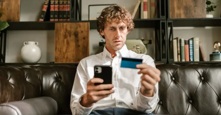 Homem no sofá usando o celular e um cartão de crédito