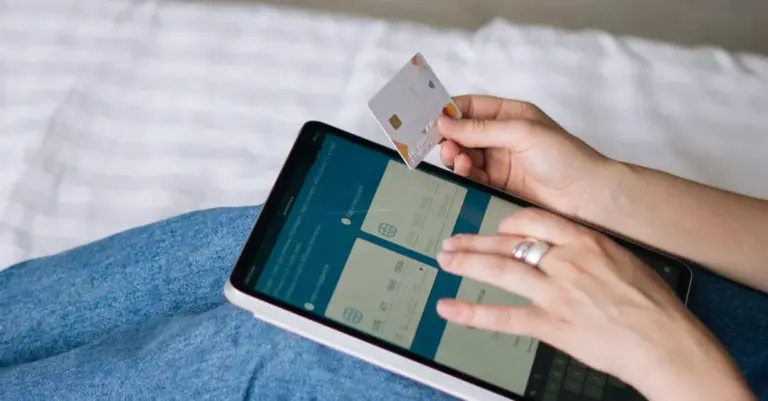 Pessoa movimentando a conta pelo app de banco no celular com o cartão em mãos