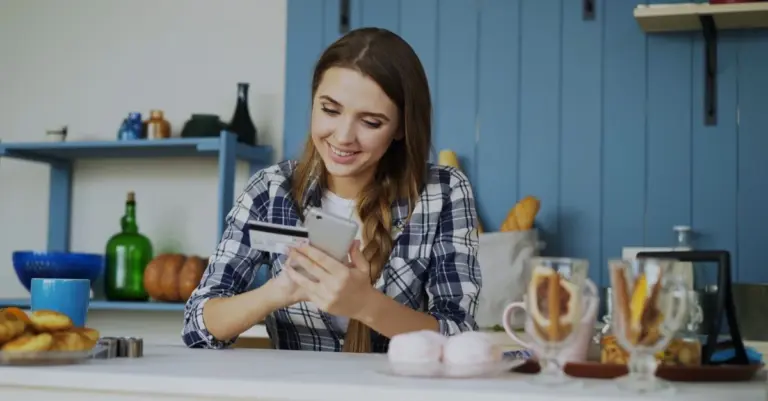 Mulher sorrindo usando o celular e um cartão