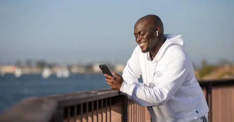 Homem sorrindo usando o celular ao ar livre