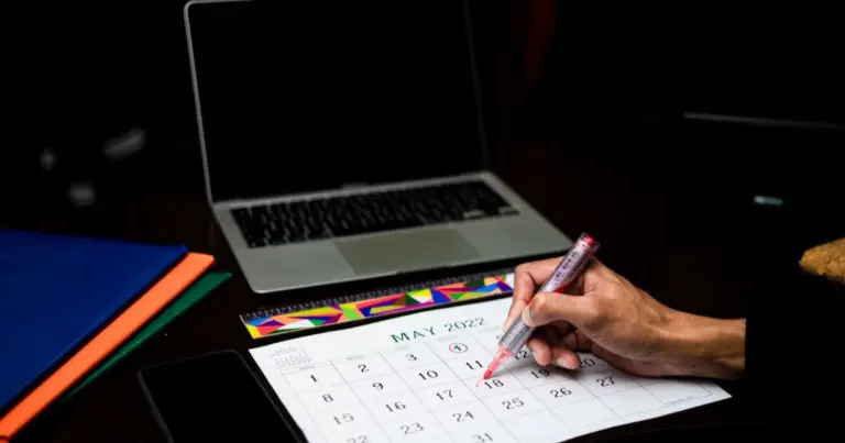 Pessoa a planear numa agenda de calendário, com portátil e telemóvel