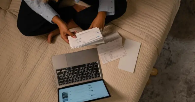 Vista superior de mulher a organizar finanças na cama com portátil e cheques