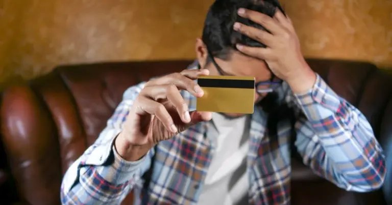 Homem com camisa aos quadrados no sofá, a segurar um cartão, com expressão de stress