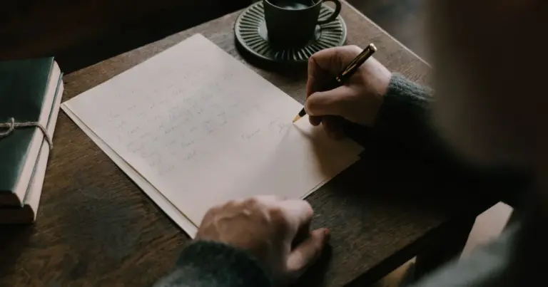 Pessoa a escrever uma carta numa secretária de madeira, com uma chávena de café