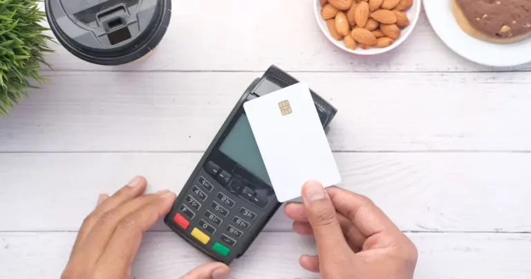 Mão a fazer pagamento contactless com cartão numa mesa de madeira