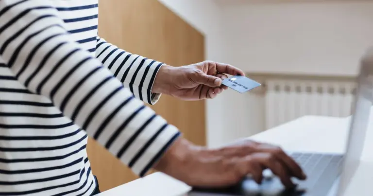 Mão a entregar um cartão de crédito enquanto usa um portátil