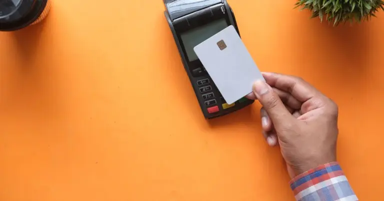 Cartão branco a ser aproximado de terminal de pagamento sobre fundo laranja