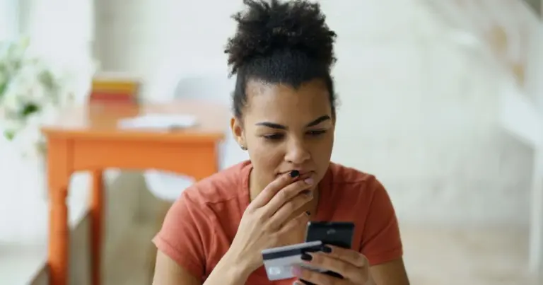 Jovem pensativa a segurar cartão e telemóvel, a decidir sobre o primeiro cartão