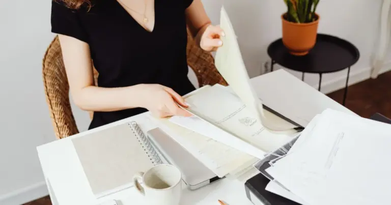 Mulher a organizar documentos e pastas numa secretária com caderno e caneca