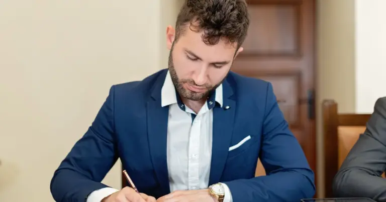 Homem confiante de fato a assinar um documento contratual numa secretária de escritório