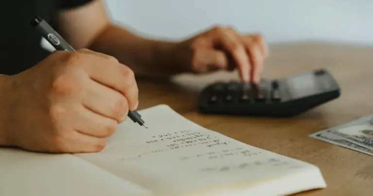 Pessoa a escrever cálculos num caderno junto a uma calculadora