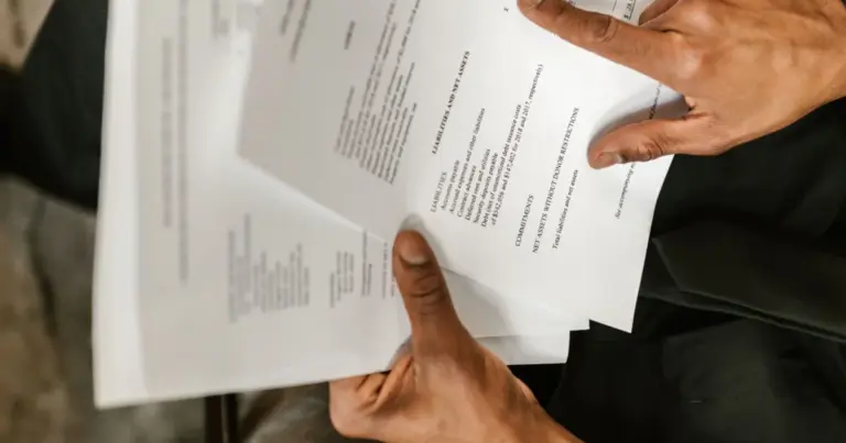 Pessoa sentada lê cuidadosamente vários documentos financeiros