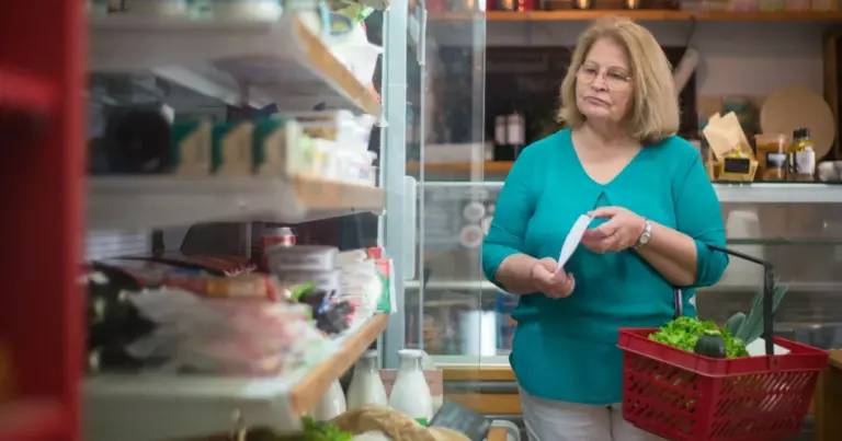 Mulher a conferir lista de compras com cesto numa mercearia