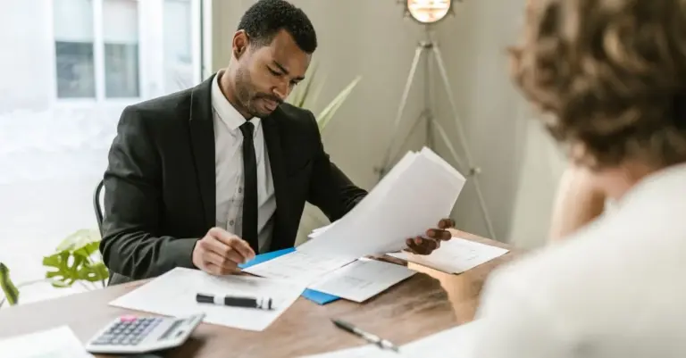 Homem de fato a analisar cuidadosamente documentos financeiros numa mesa de escritório